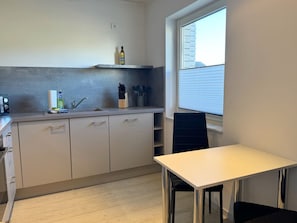 Una cocina compacta con ventana, una mesa de comedor y una silla negra.