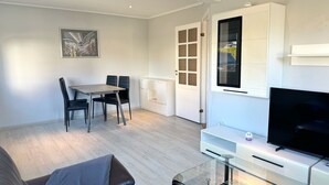 A modern living room with a glass coffee table, a flat-screen TV, a sofa, and a dining area with a table and chairs. - ETW Hausberg 45 - Fr. Schwenn - Großzügiges Ferienappartement in Ruhiger Wohnsiedlung (Sassnitz)