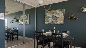 Un comedor con una mesa de vidrio, sillas oscuras y un cuadro abstracto grande en la pared.