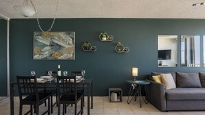 Un comedor con una mesa preparada para cuatro personas, un sofá y una pequeña mesita de noche con una lámpara.