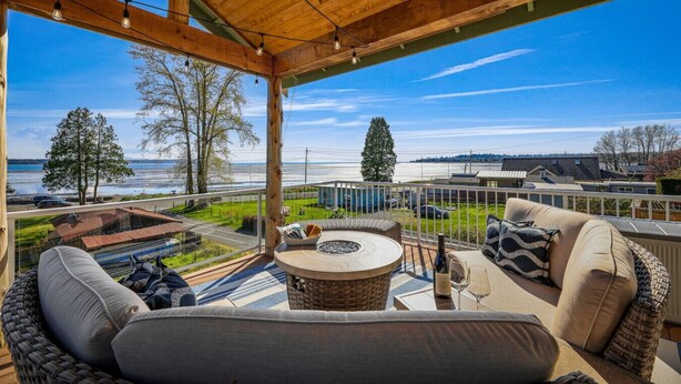A covered outdoor seating area with a view of a body of water, a fire pit, and a dining table. - The Perch | Birch Bay Views · Fire Deck · Beach (Blaine)