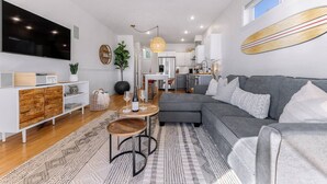 A modern living room with a grey sofa, wooden coffee table, and a TV mounted on the wall. - The Perch | Birch Bay Views · Fire Deck · Beach (Blaine)