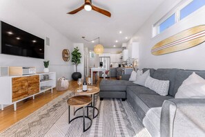 Ein modernes Wohnzimmer mit grauem Sofa, einem Holztisch und einem an der Wand befestigten Fernseher.