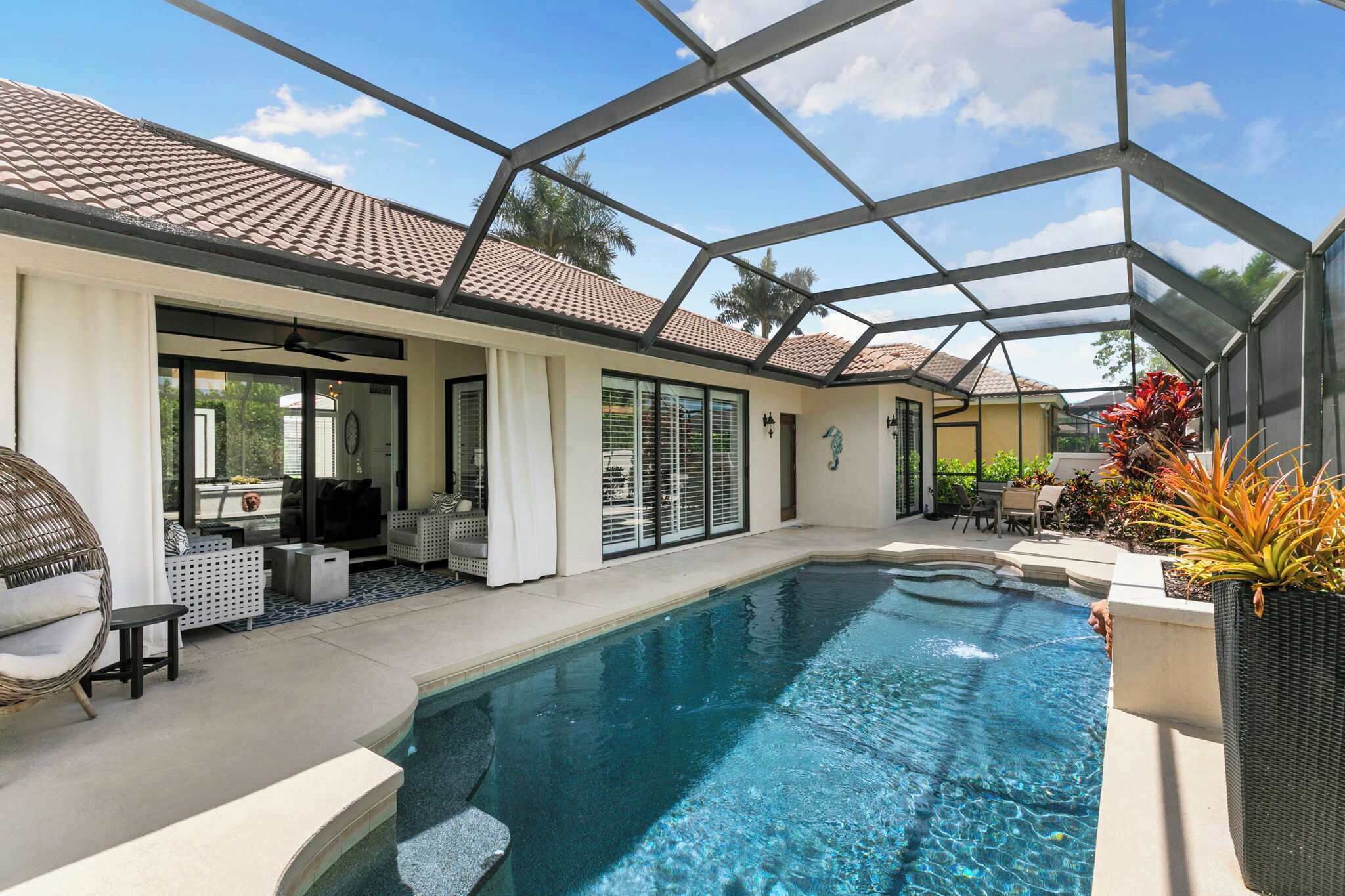 Uma área de piscina com um terraço envidraçado, mobiliário de exterior e céu azul.