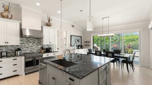 A modern kitchen with a large island, stainless steel appliances, and a view to the outdoors. - 3BR Ritzy Marco Home l Lush Heated Pool (Marco Island)