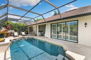 A swimming pool with a glass enclosure, outdoor seating, and a covered patio area. - 3BR Ritzy Marco Home l Lush Pool (Marco Island)