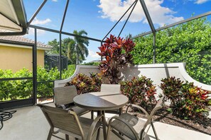 A covered outdoor seating area with a table and chairs, surrounded by greenery and a view of the sky. - 3BR Ritzy Marco Home l Lush Pool (Marco Island)