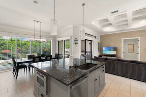 A modern kitchen with a central island, a dining area with a table and chairs, and a living area with a sofa and TV.