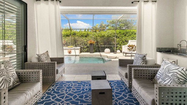 A modern outdoor living area with a pool, seating, and a view of greenery.