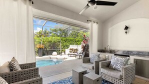 A modern outdoor living area with a pool, lounge chairs, and a kitchen area. - 3BR Ritzy Marco Home l Lush Heated Pool (Marco Island)