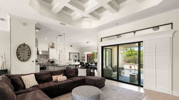 A modern living room with a sectional sofa, ottoman, and a large wall clock. - 3BR Ritzy Marco Home l Lush Heated Pool (Marco Island)