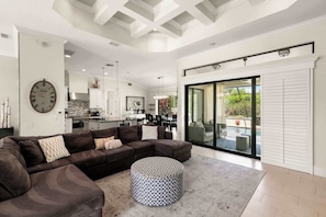 A modern living room with a sectional sofa, ottoman, and a large wall clock. - 3BR Ritzy Marco Home l Lush Pool (Marco Island)