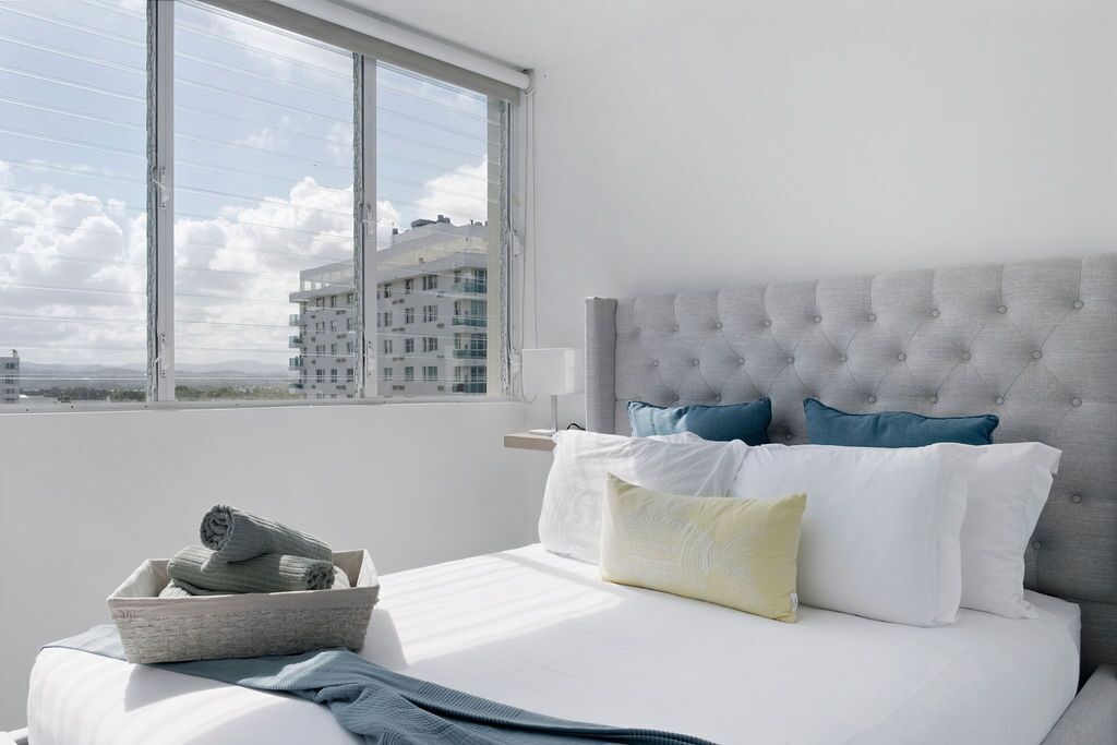 A hotel room with a bed, a window, and a view of buildings.