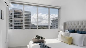 A bedroom with a large window, a bed with white bedding, and a headboard. - Flamenco Beach 2BDR Oceanfr Pool Parking (Carolina)
