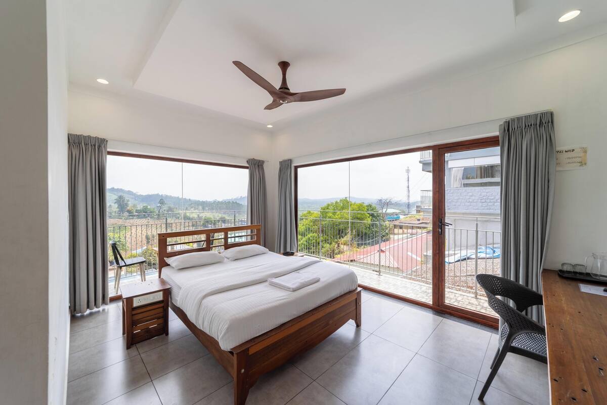A modern bedroom with a large bed, a desk, and a view of the outdoors.