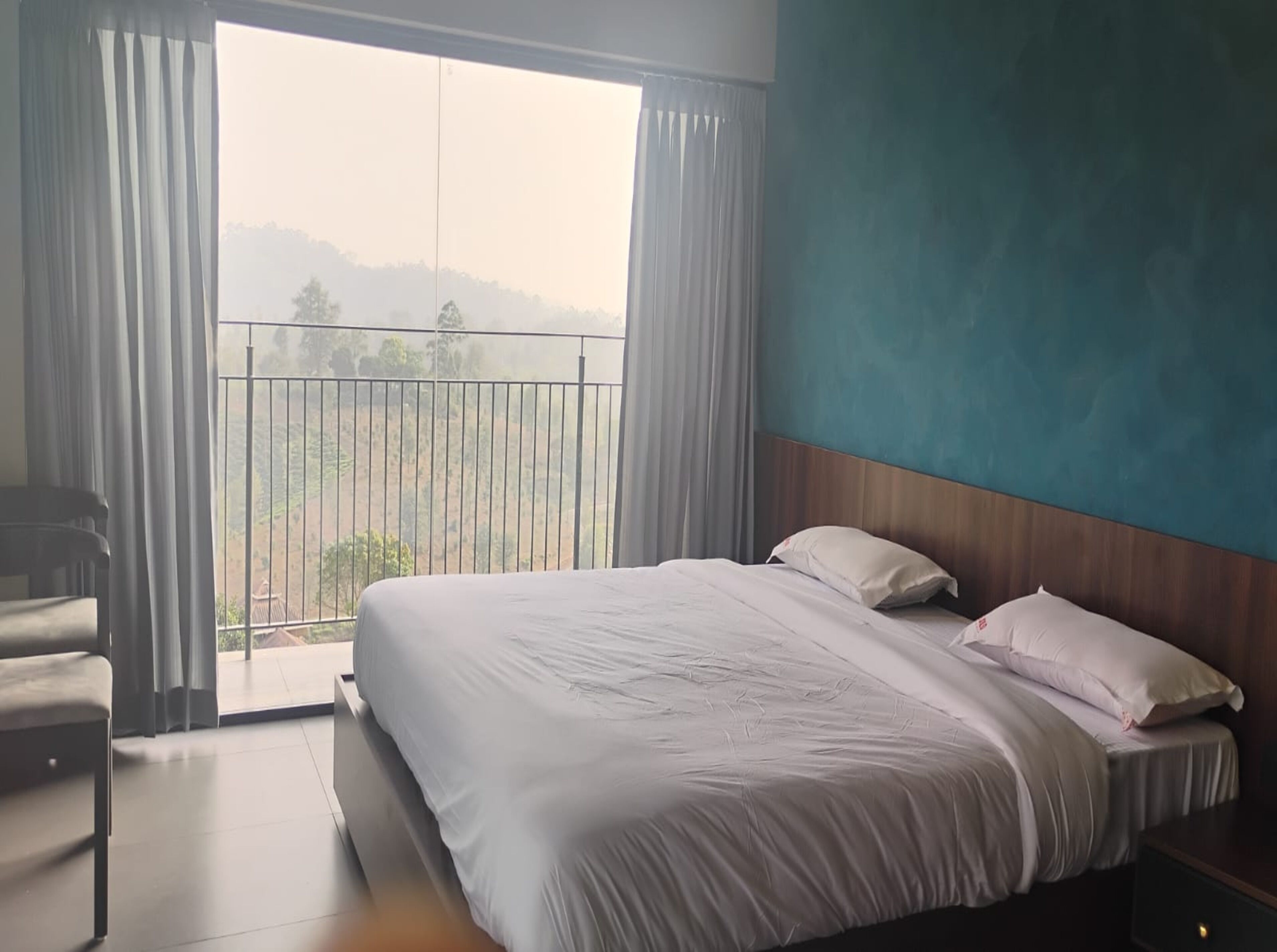 A hotel room with a large bed, a chair, and a balcony with a view of the countryside.