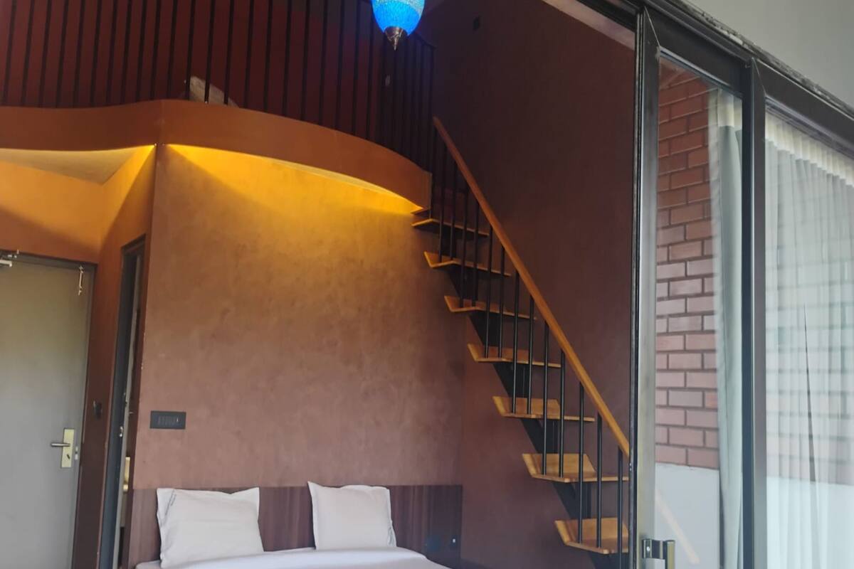 A modern bedroom with a curved wall, a wooden staircase, and a large bed.