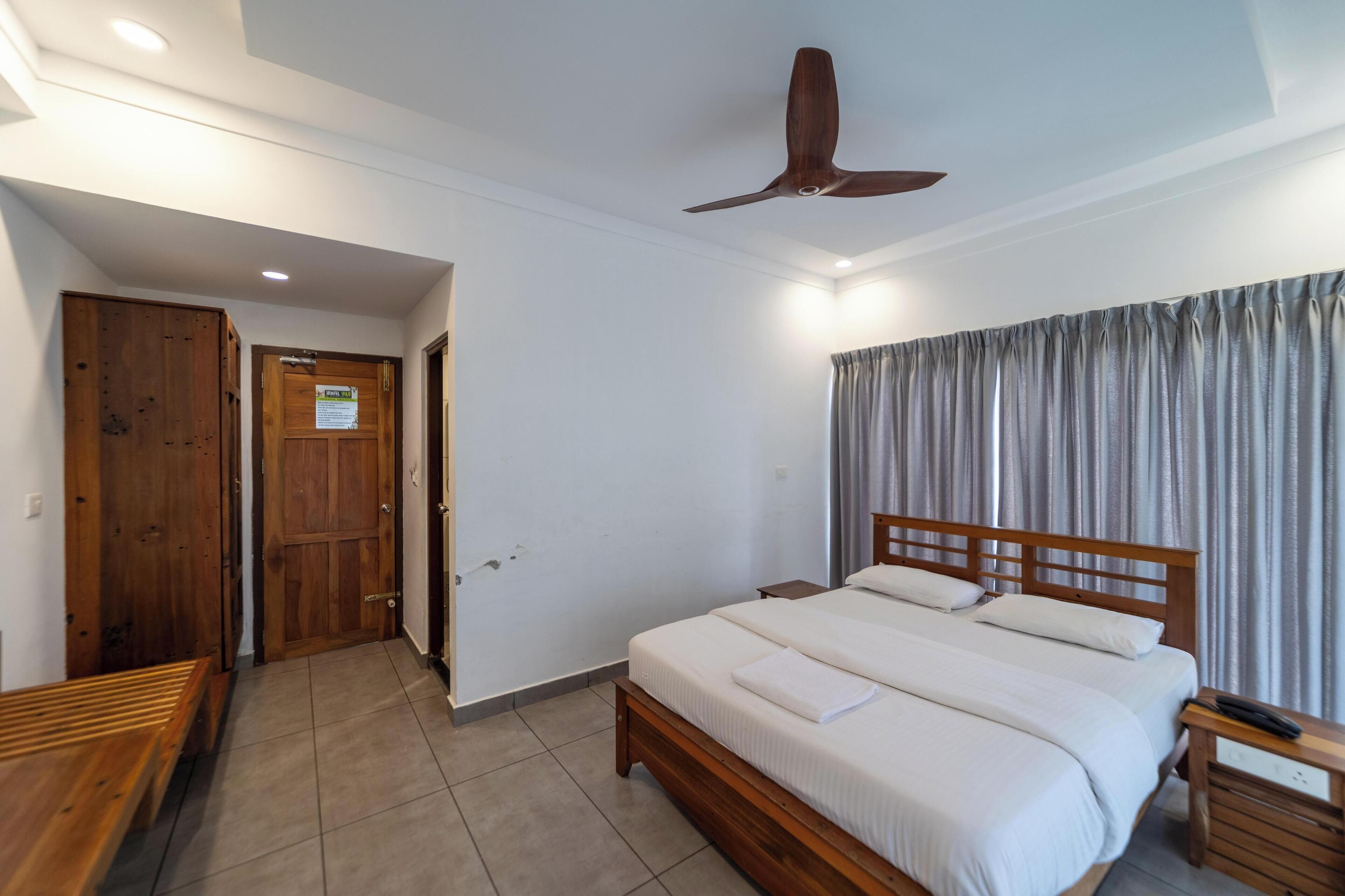 Un dormitorio con una cama de madera, un ventilador de techo y vistas al exterior a través de una ventana con cortinas.
