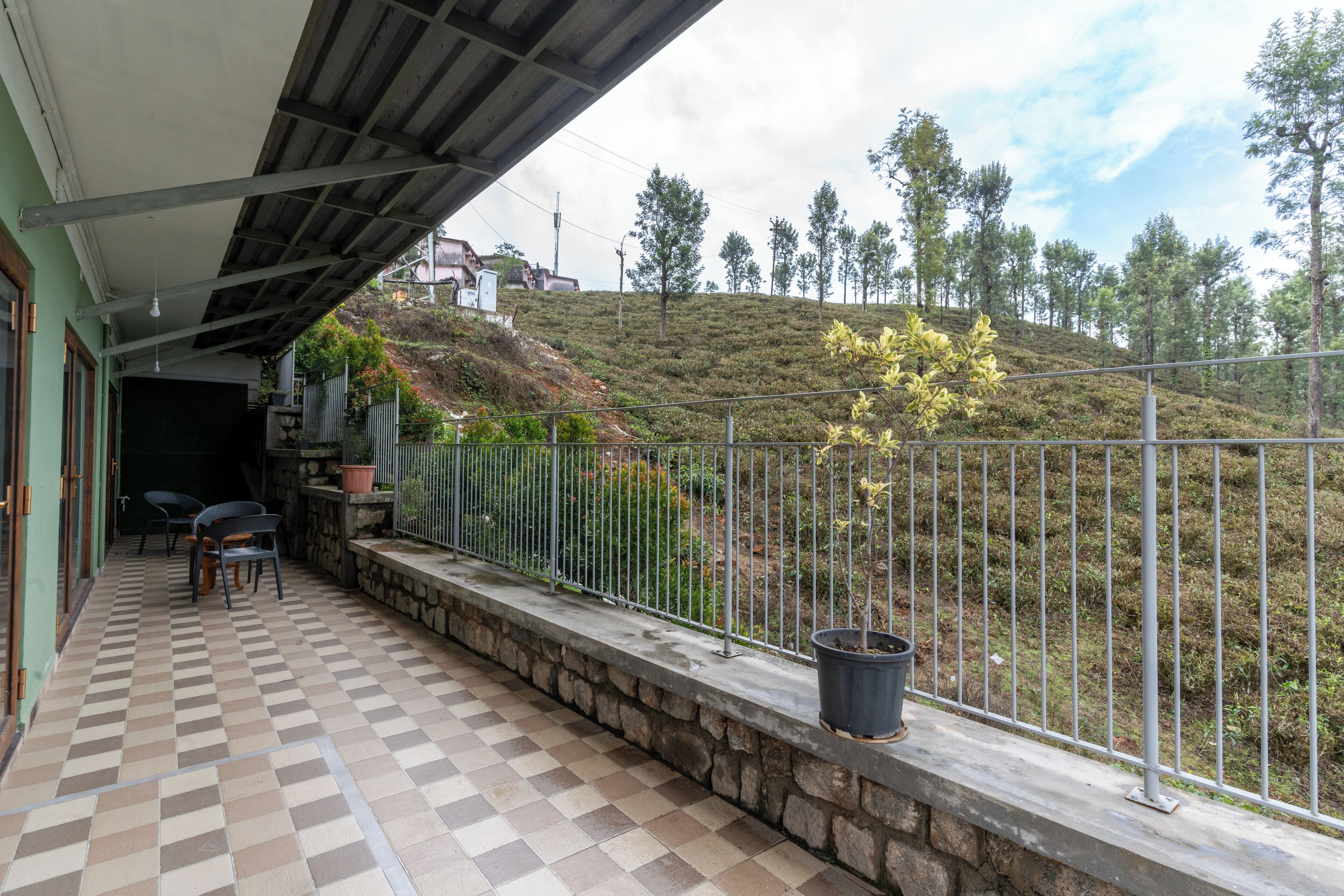 A balcony with a checkered floor, a stone wall, and a metal railing overlooking a hilly landscape with trees.