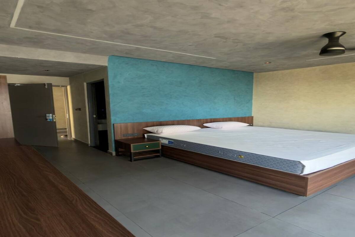 A modern hotel room with a large bed, a wooden nightstand, a small drawer, and a ceiling fan.