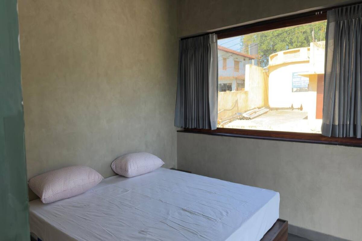A single bed with two pillows in a room with a window overlooking a building.