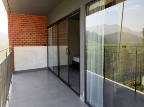 Un balcon avec une porte vitrée donnant sur une chambre, un mur en briques et une vue sur un paysage montagneux.