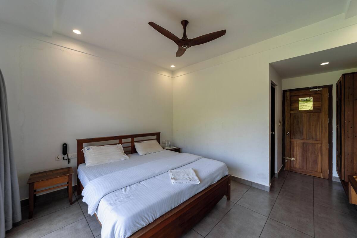 A bedroom with a single bed, a wooden nightstand, a ceiling fan, and a wooden door.