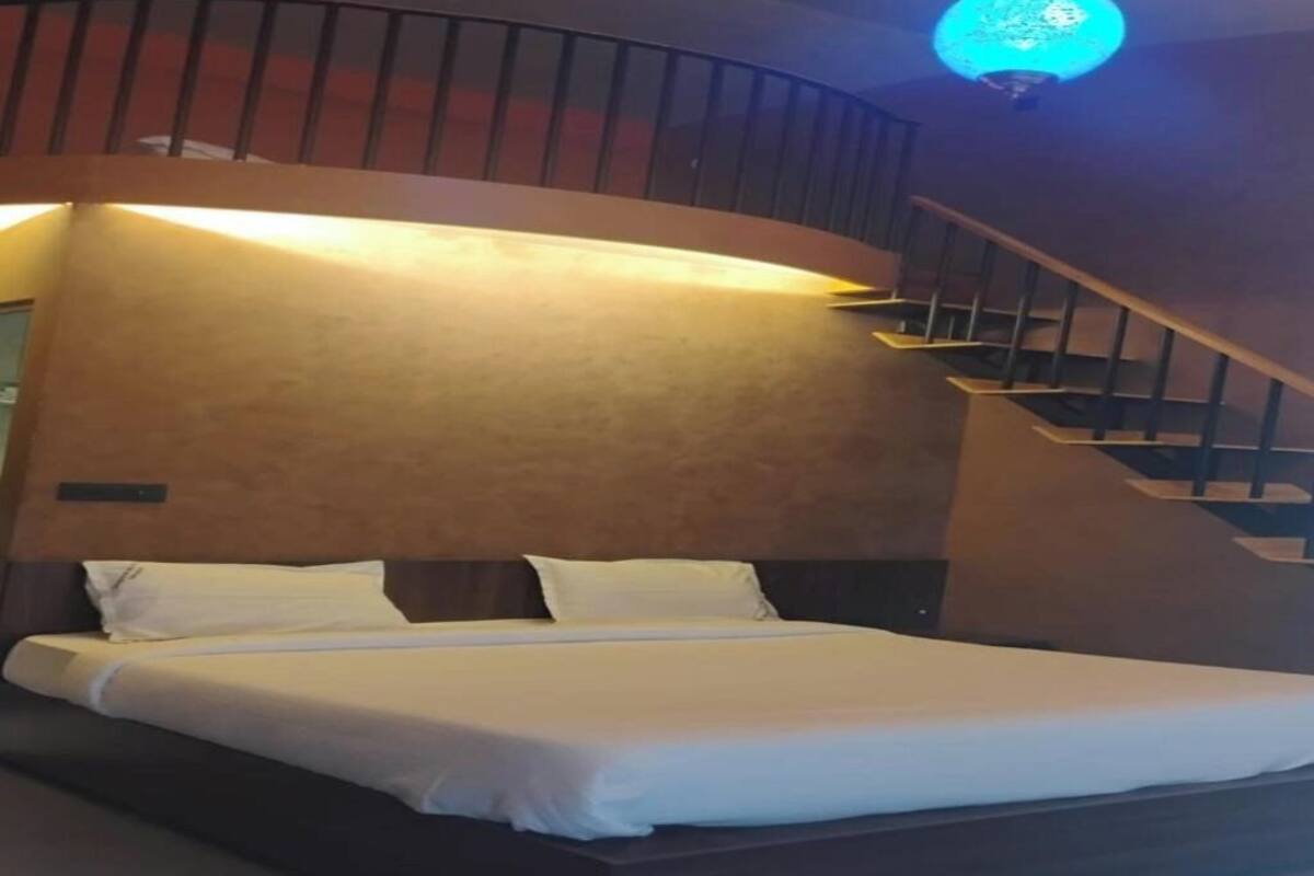 A modern hotel room with a curved staircase, a large bed with white linens, and a unique ceiling light fixture.