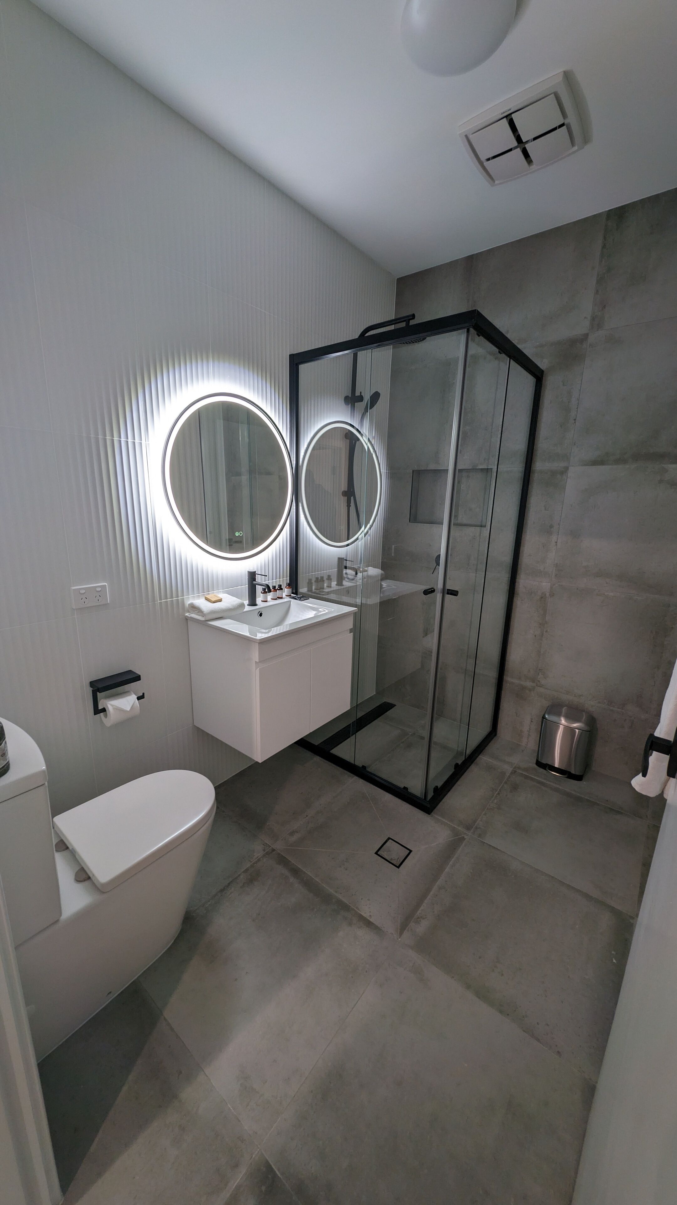 A modern bathroom with a glass shower enclosure, a white sink, and two illuminated mirrors.