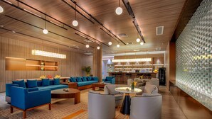 Um lobby moderno com um sofá azul, uma mesa de centro e uma área de bar ao fundo.