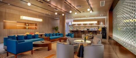 A modern lobby with a blue sofa set, a coffee table, and a bar area in the background.