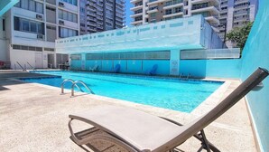 Una piscina con sillones de descanso y vistas despejadas a edificios altos al fondo.