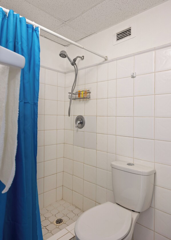 A small bathroom with a shower, toilet, and a shelf with toiletries. - Playa Mujeres 1BDR Oceanfr Pool Parking (Carolina)