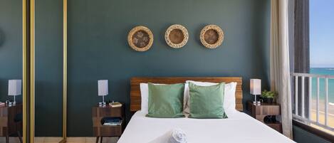 A hotel room with a large bed, green walls, and a view of the sea.