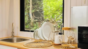 Eine Küche mit einer Edelstahlspüle, einem Fenster mit Blick auf Grünflächen sowie einer Arbeitsplatte mit Geschirrgestell, Kaffeemaschine und Weingläsern.