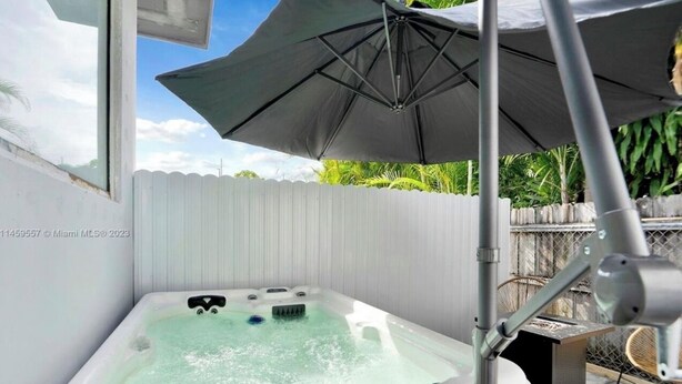 A hot tub with a canopy, a metal chair, and a white fence in the background. - HOT TUB + WASHER AND DRYER in Unit / MIAMI (Miami)