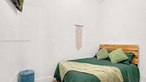 A bedroom with a bed, green bedding, a wooden headboard, a wall hanging, and a blue cylindrical object. - HOT TUB + WASHER AND DRYER in Unit / MIAMI (Miami)