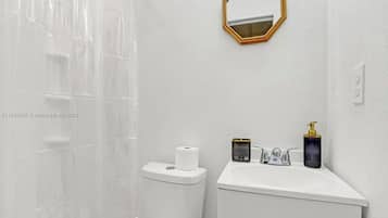 Un baño con inodoro blanco, lavabo con dispensador de jabón y cortina de ducha.