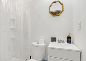 Une salle de bain avec des toilettes blanches, un lavabo doté d’un distributeur de savon et un rideau de douche.
