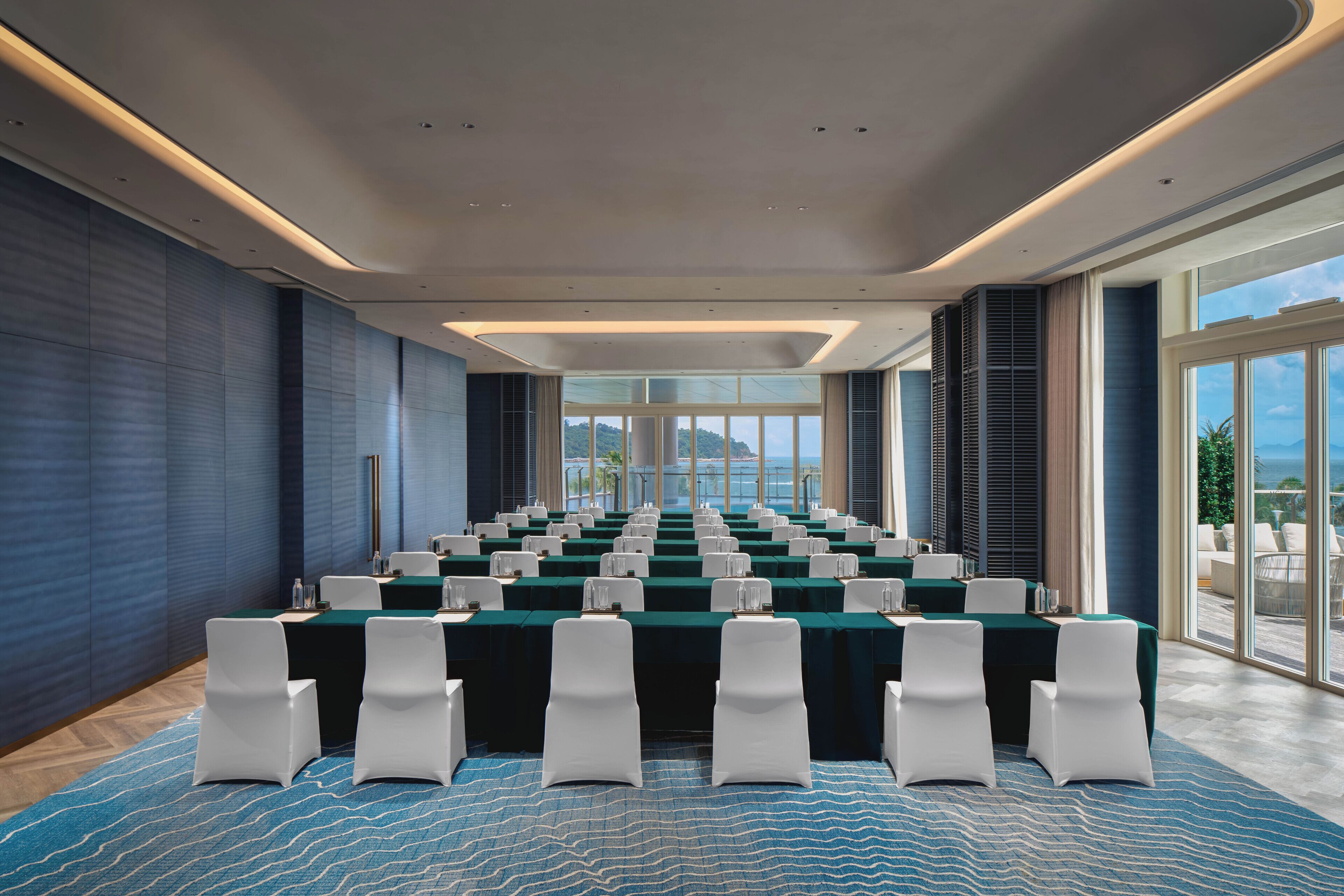 Un salón de conferencias con una larga mesa, sillas blancas y una alfombra azul.