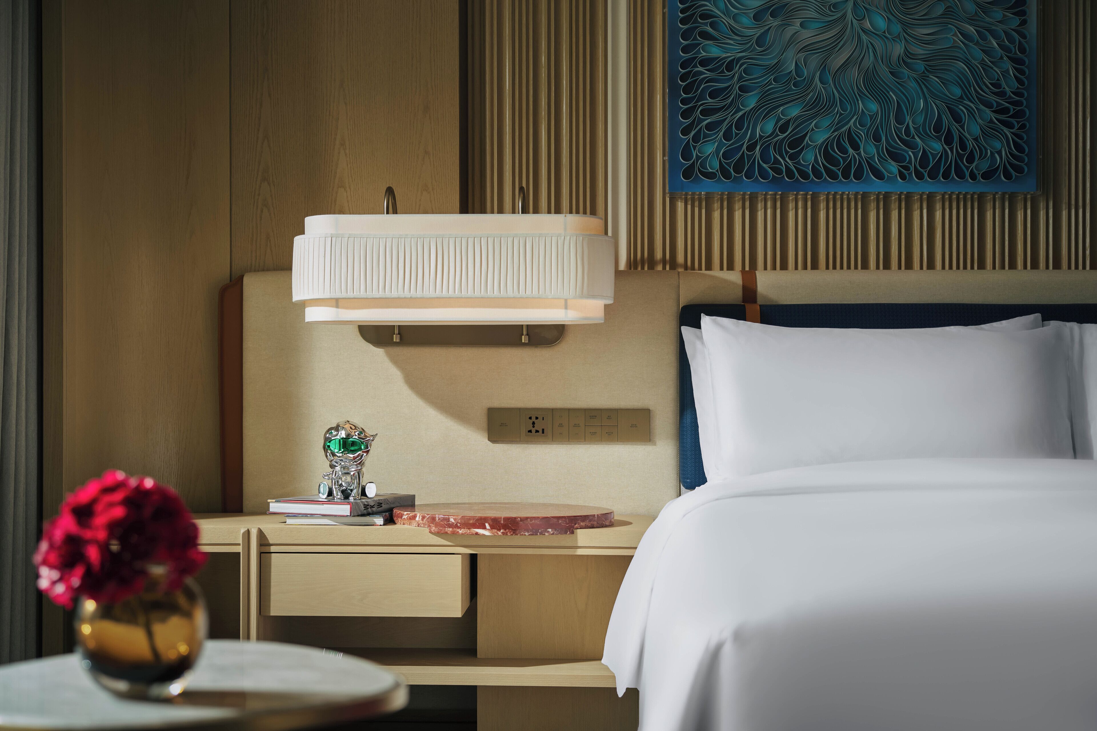 A hotel room with a bed, bedside table, lamp, and artwork on the wall.