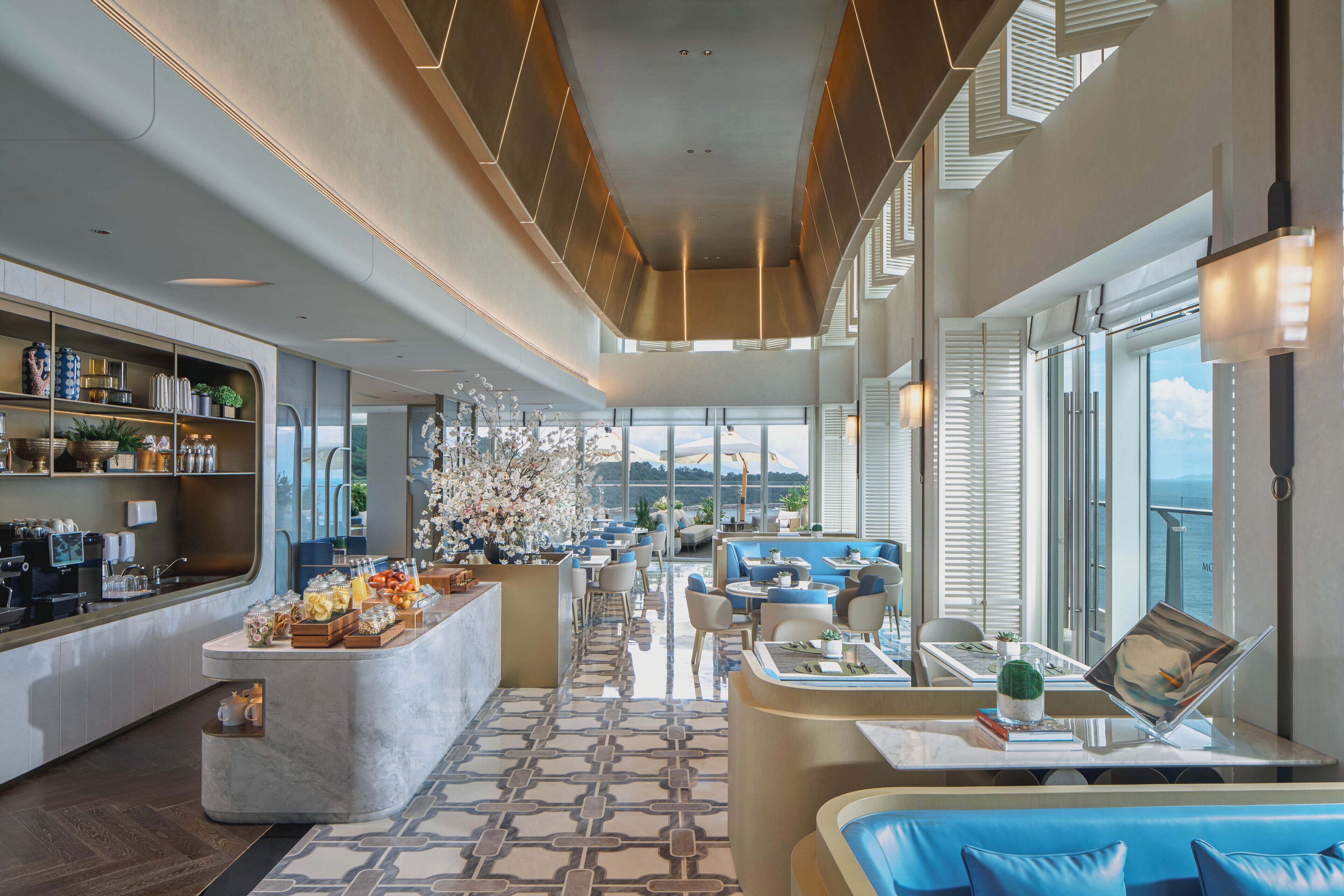 Un lobby moderno de hotel con una barra central, espacios para sentarse y grandes ventanales con vistas.
