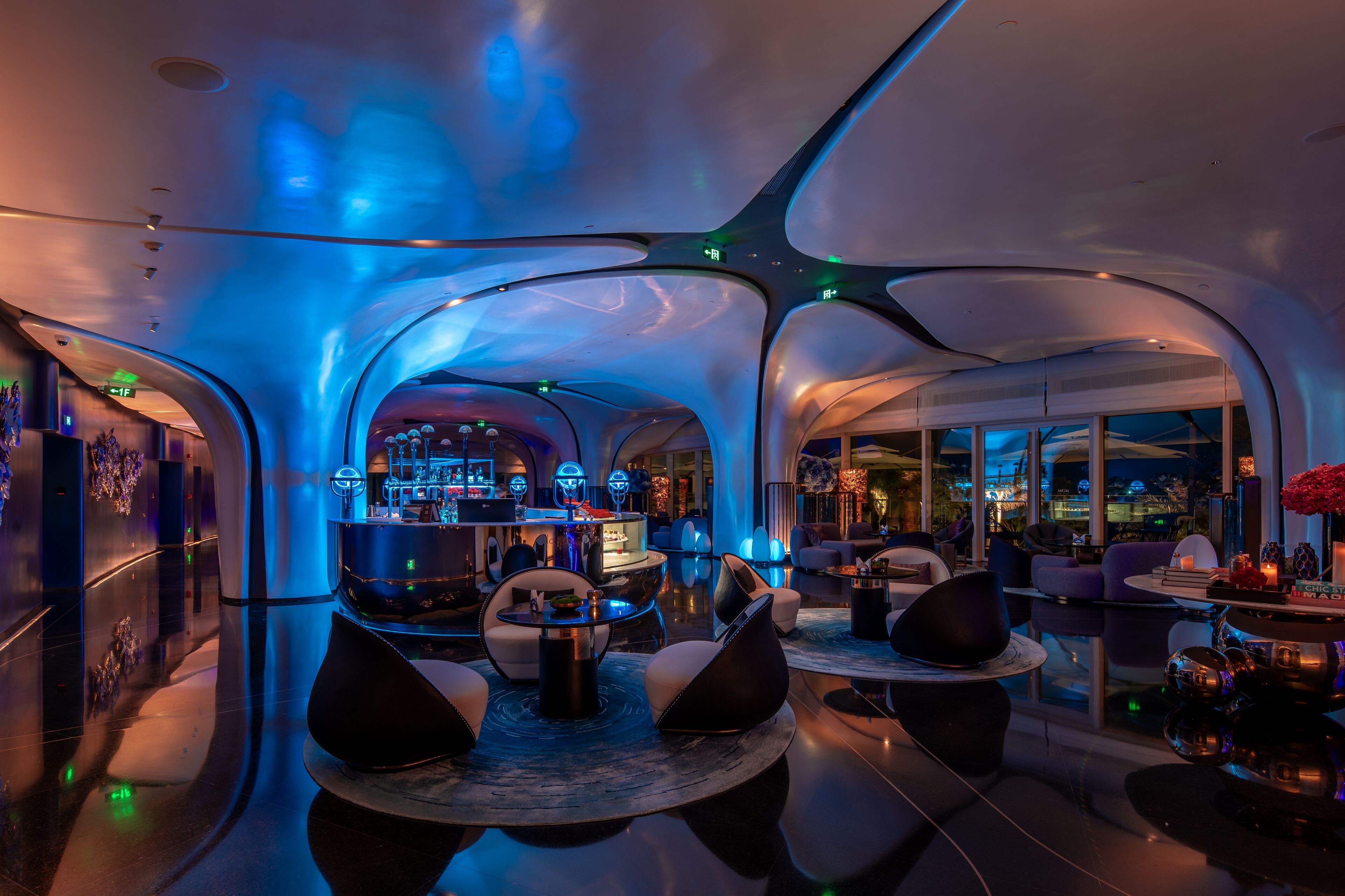 A modern, spacious lobby with a bar area, comfortable seating, and large windows offering a view of the cityscape.