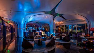 A modern, spacious lobby with a bar area, comfortable seating, and large windows offering a view of the cityscape.