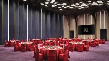 Une salle de conférence avec des tables rondes, des chaises rouges et un grand écran affichant du texte.