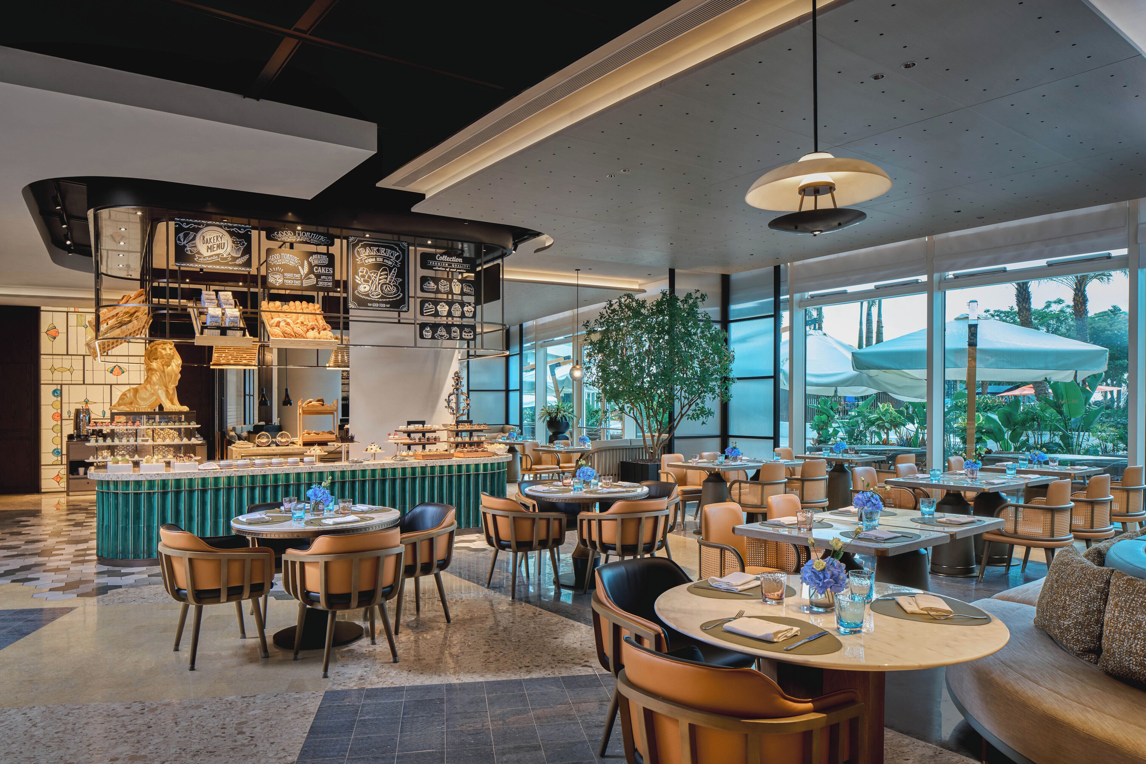 En modern restaurang med en central bar, runda bord och stolar samt stora fönster med utsikt över palmer.