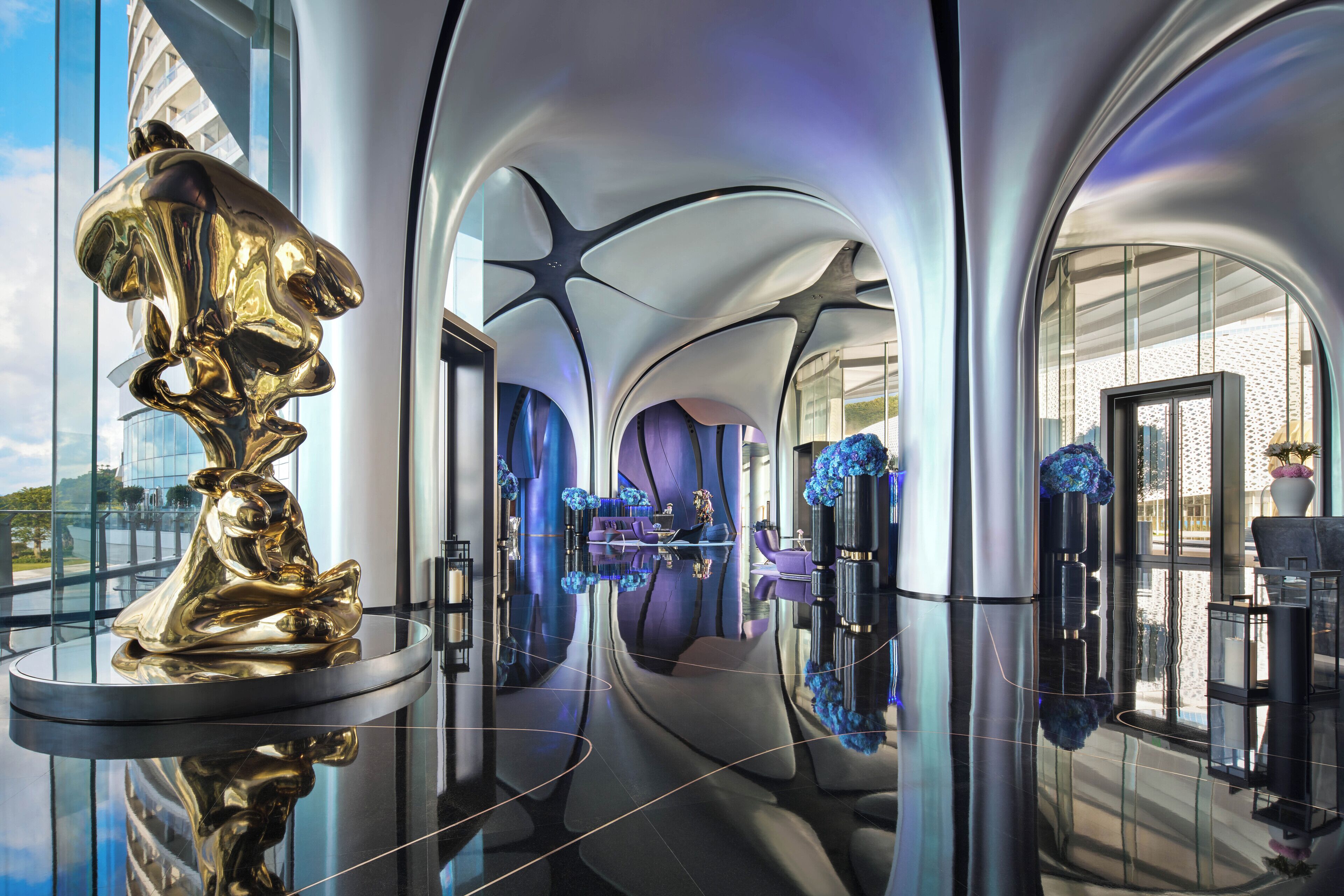A modern interior with a reflective floor, a central seating area, and a large gold sculpture.