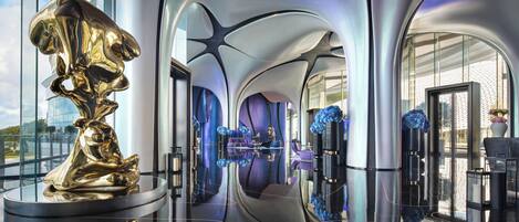 A modern interior with a reflective floor, a central seating area, and a large gold sculpture.