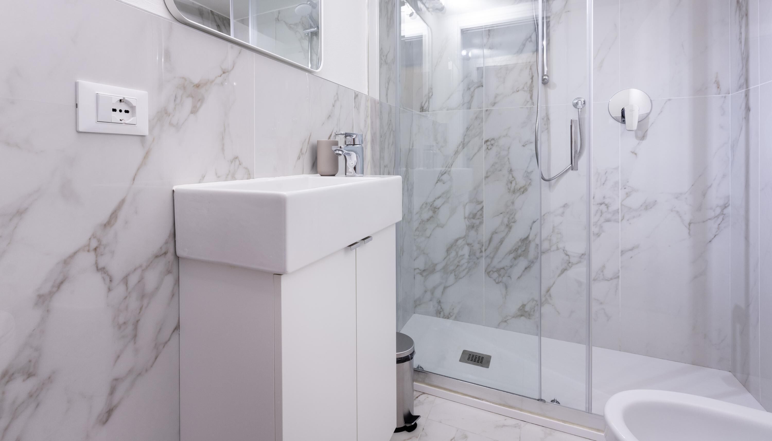 Une salle de bain moderne avec un lavabo en marbre, une douche à parois de verre et une baignoire blanche.