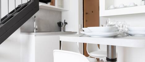 A modern kitchen with white cabinetry, a stainless steel sink, and a dining area with white chairs and a table set for two.
